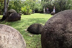 A view of Parque de las Esferas in Palmar Sur, Costa Rica, showing a pathway leading through the park with several large stone spheres scattered throughout the landscape.